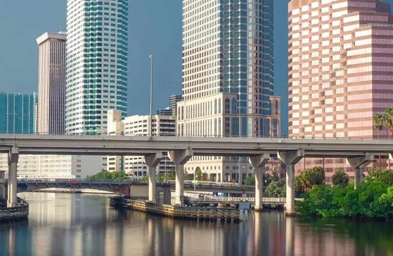 Urban cityscape featuring modern high-rise buildings, elevated highway, and reflective river.