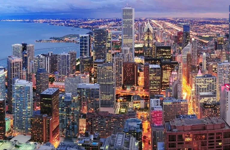 Aerial view of a city skyline at dusk with illuminated skyscrapers and streets.