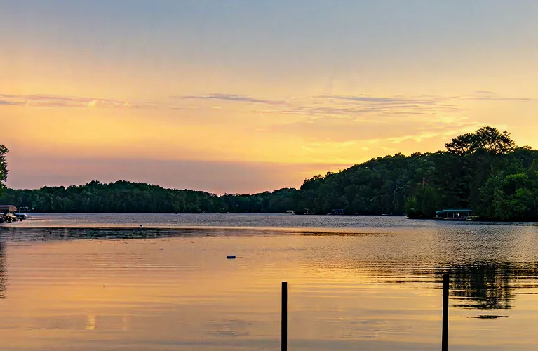 Tranquil lake at sunset with golden sky, calm water, and tree-covered shoreline.
