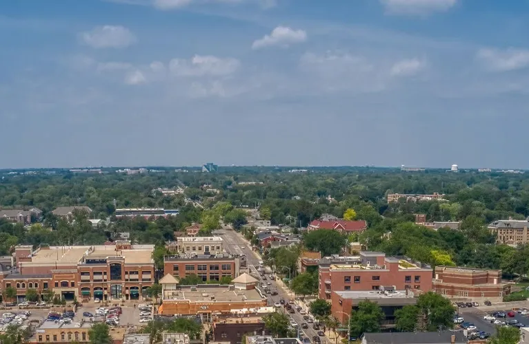 Aerial view of a mid-sized urban area with brick buildings, roads, greenery, and a partly cloudy sky.