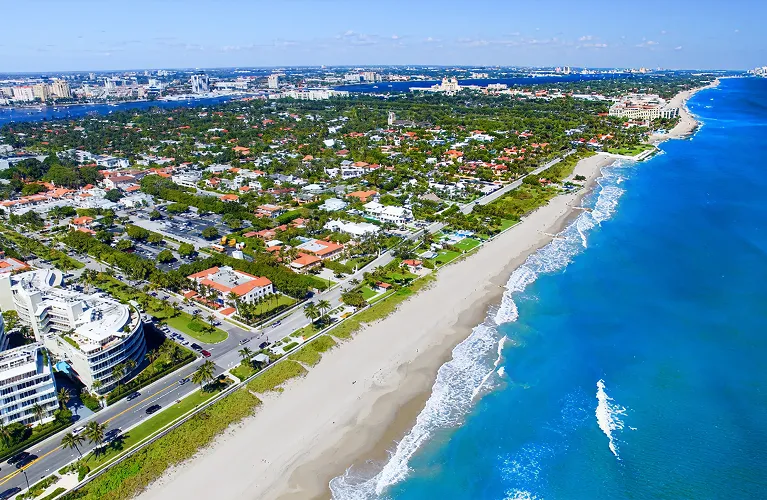 Aerial view of a coastal city with sandy beach, blue ocean, and residential buildings.