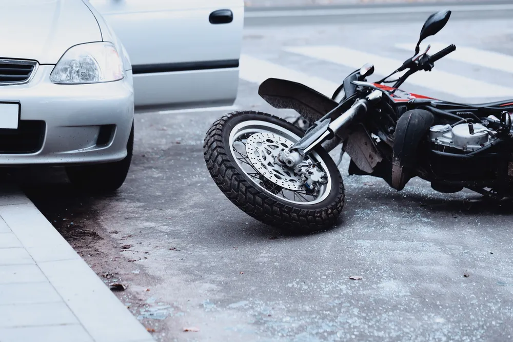 White car with open door and fallen black motorcycle on asphalt street.
