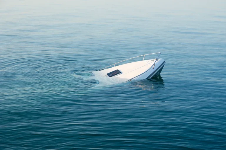 Partially submerged white motorboat tilted in calm blue water.