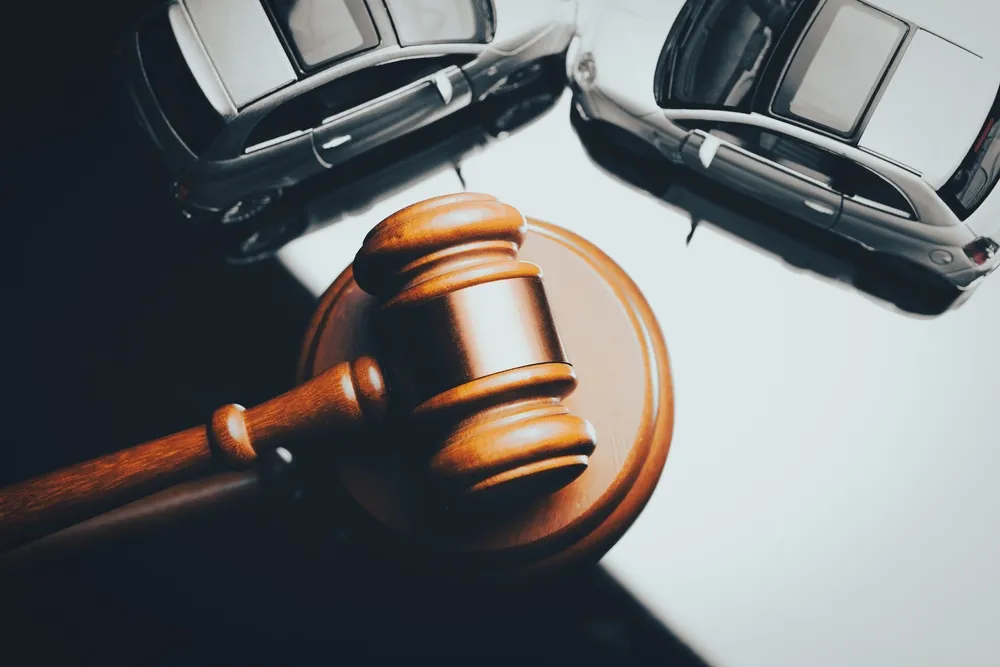 Wooden judge's gavel next to two silver model cars on a white and dark background.
