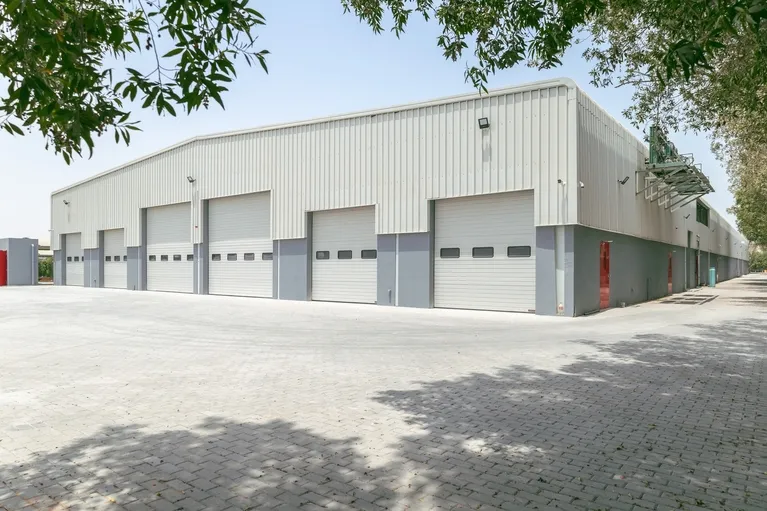 Exterior view of a large industrial warehouse with multiple closed white roll-up doors.