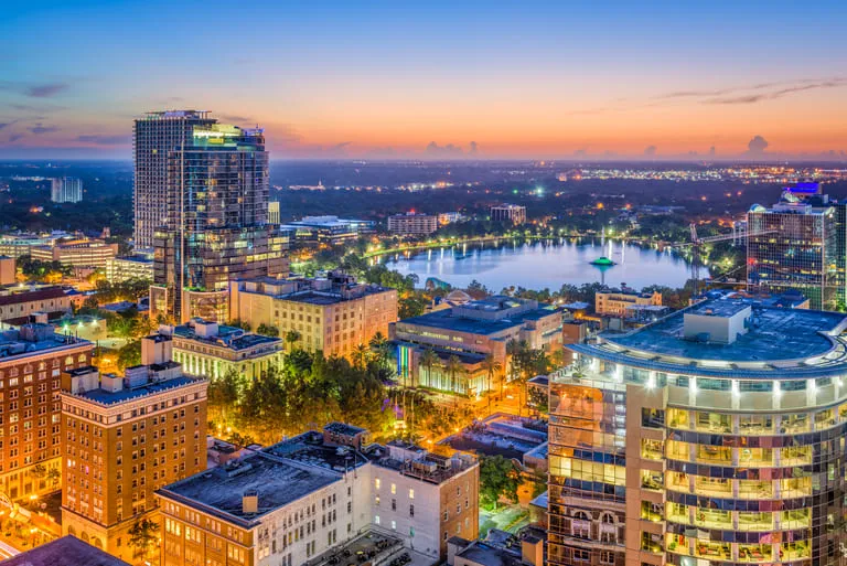 Aerial view of a cityscape at dusk with illuminated buildings and a large lake.