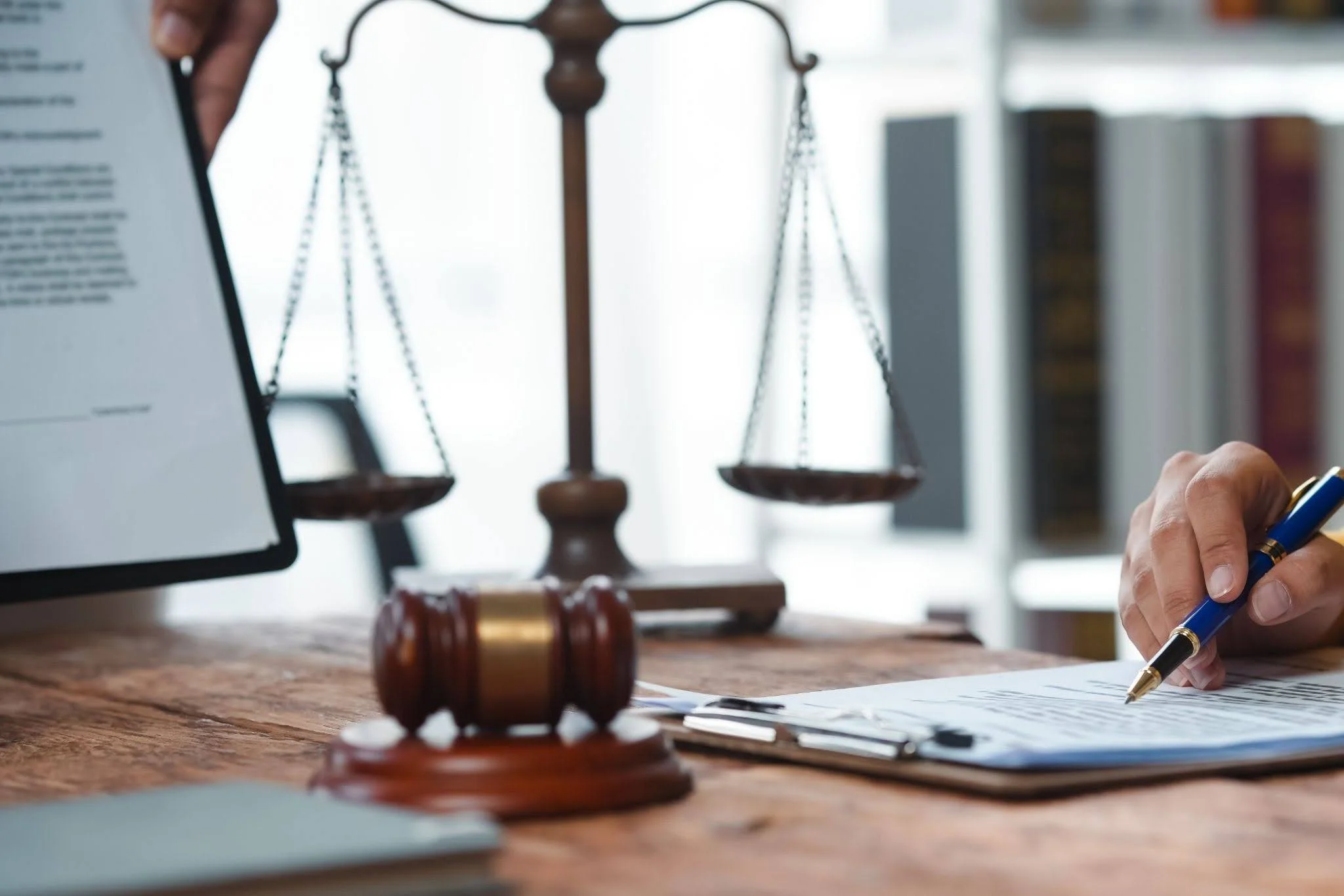 Close-up of a legal document being signed, with a gavel and scales of justice in the background.
