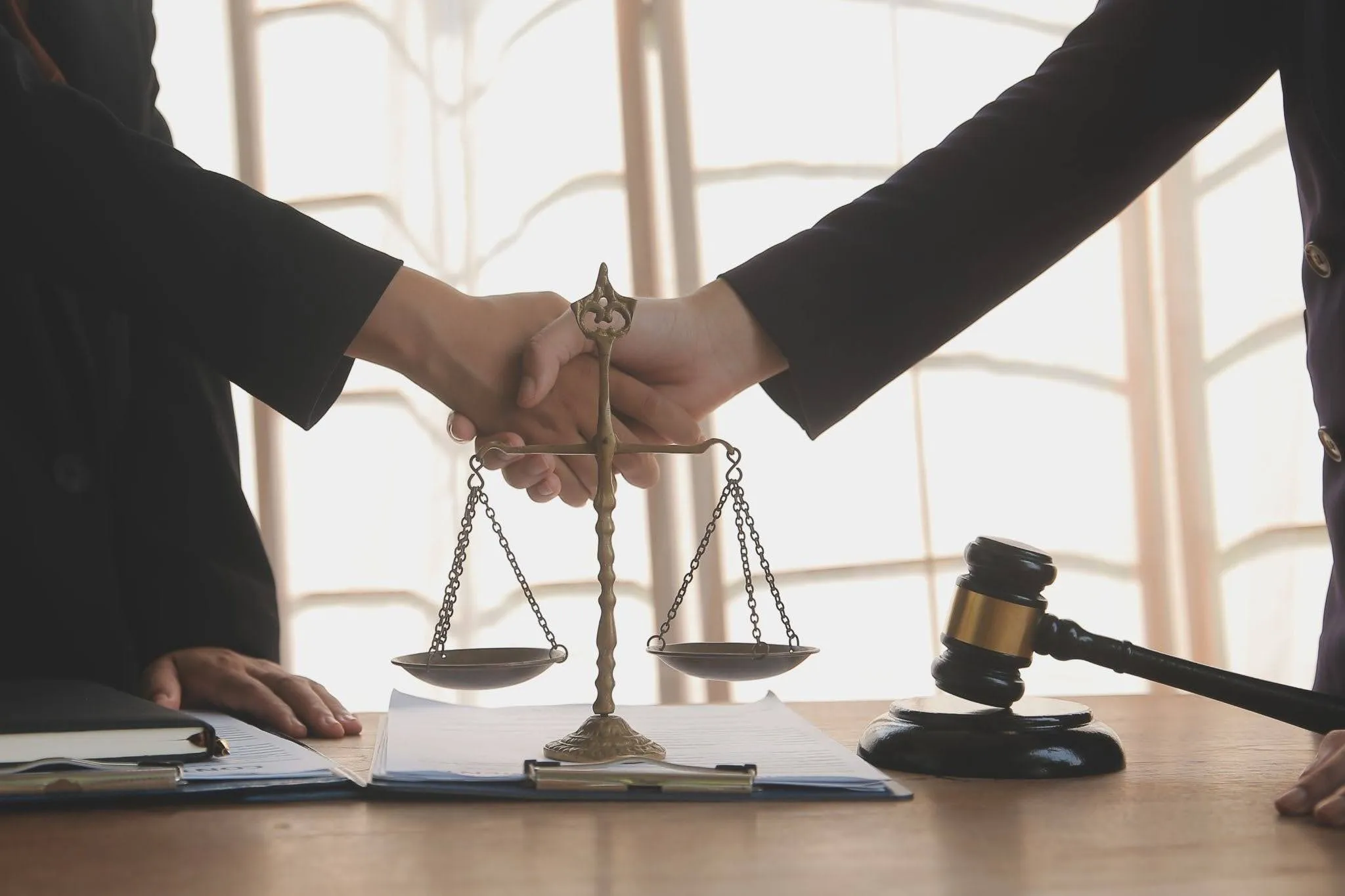 Two professionals shaking hands over a desk with scales of justice and a gavel.
