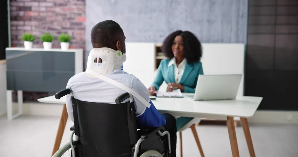 Man in wheelchair wearing neck brace consulting female professional at office desk